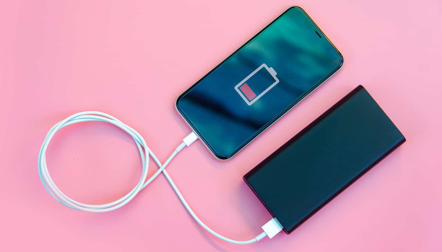 Flatlay sur un fond rose d'un smartphone en charge grâce à une batterie externe.