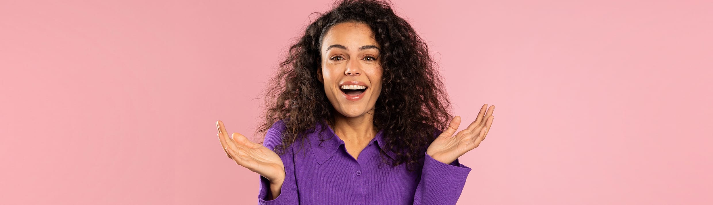 Een vrouw op een roze achtergrond die vragend haar handen in de lucht heeft.