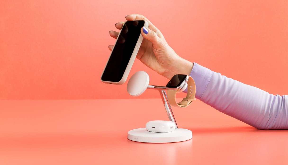 Een hand komt van rechts en klikt een telefoon magnetisch op een oplaadstation.