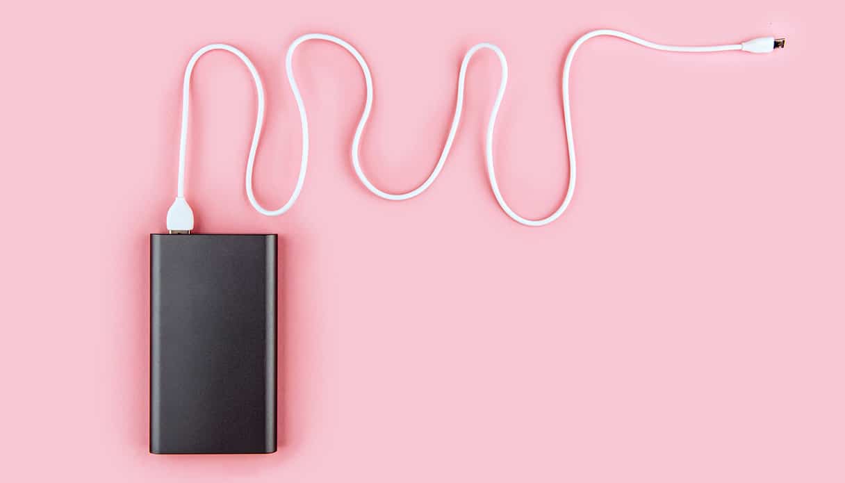 Un homme est allongé sur un sac à dos et regarde son téléphone pendant qu'il est chargé par une batterie externe.