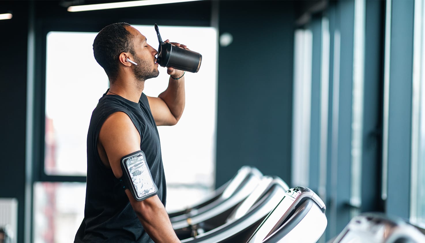 Un homme se tient sur un tapis de course avec des Apple AirPods Pro dans les oreilles en écoutant de la musique.