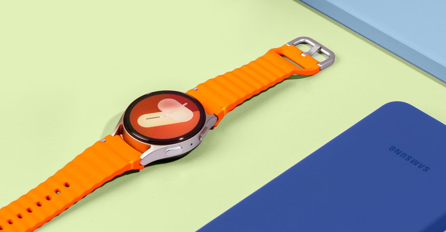 Foto van een Samsung Galaxy Watch met oranje bandje op een gele achtergrond. 